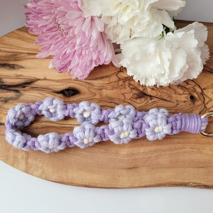 Purple and Lilac Flower Macrame Wristlet Keychain with gold clip, laying on a piece of wood