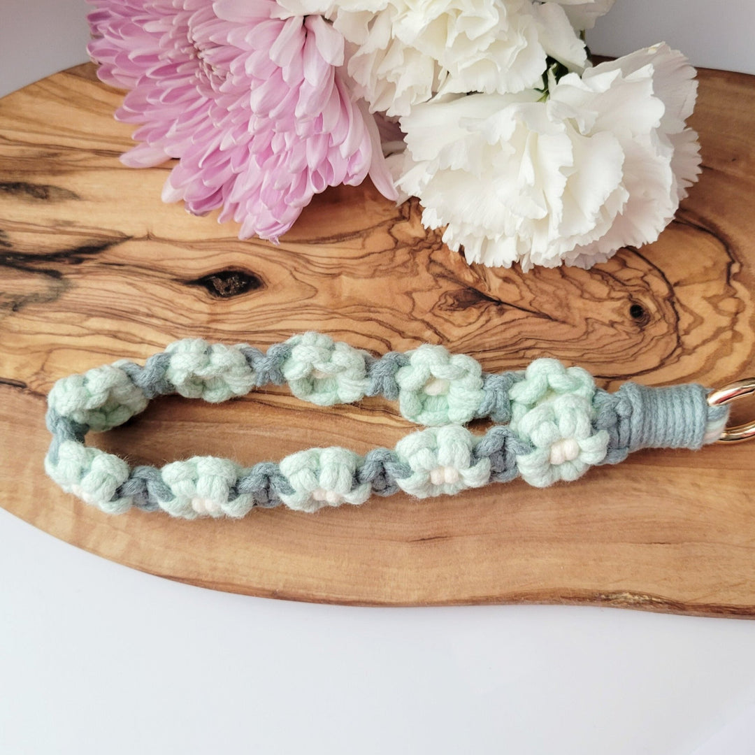 Teal and Blue Flower Macrame Wristlet Keychain with gold clip, laying on a piece of wood