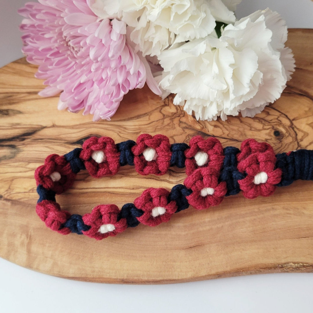 Blue and Maroon Flower Macrame Wristlet Keychain with gold clip hanging on hand lying on a wooden board