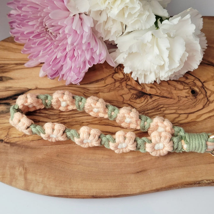 Sage and Pink Flower Macrame Wristlet Keychain with gold clip, laying on a piece of wood