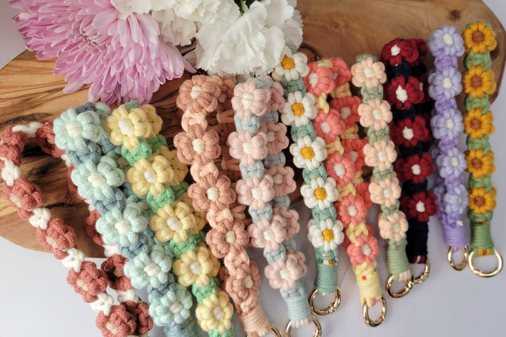 Blue and Maroon Flower Macrame Wristlet Keychain with gold clip, laying in a row with 10 other wristlet keychains, all in multiple colors