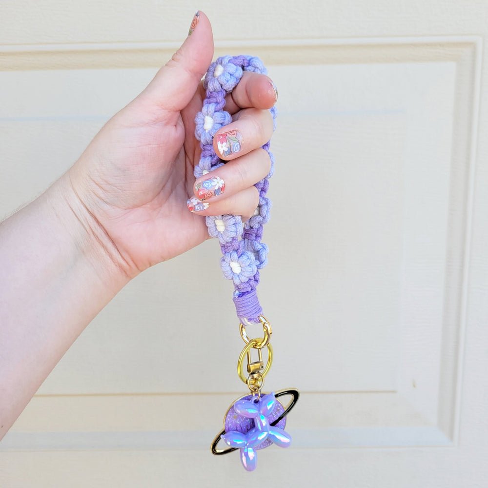 Purple and Lilac Flower Macrame Wristlet Keychain with gold clip, being held in one hand, hanging in the air with several keychains attached