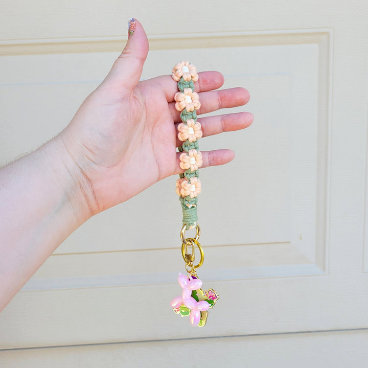 Sage and Pink Flower Macrame Wristlet Keychain with gold clip, being held in one hand, hanging in the air with several keychains attached