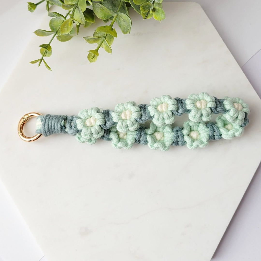 Teal and Blue Flowers Macrame Wristlet Keychain with gold clip, laying on a tile