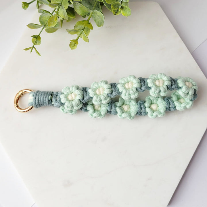 Teal and Blue Flowers Macrame Wristlet Keychain with gold clip, laying on a tile
