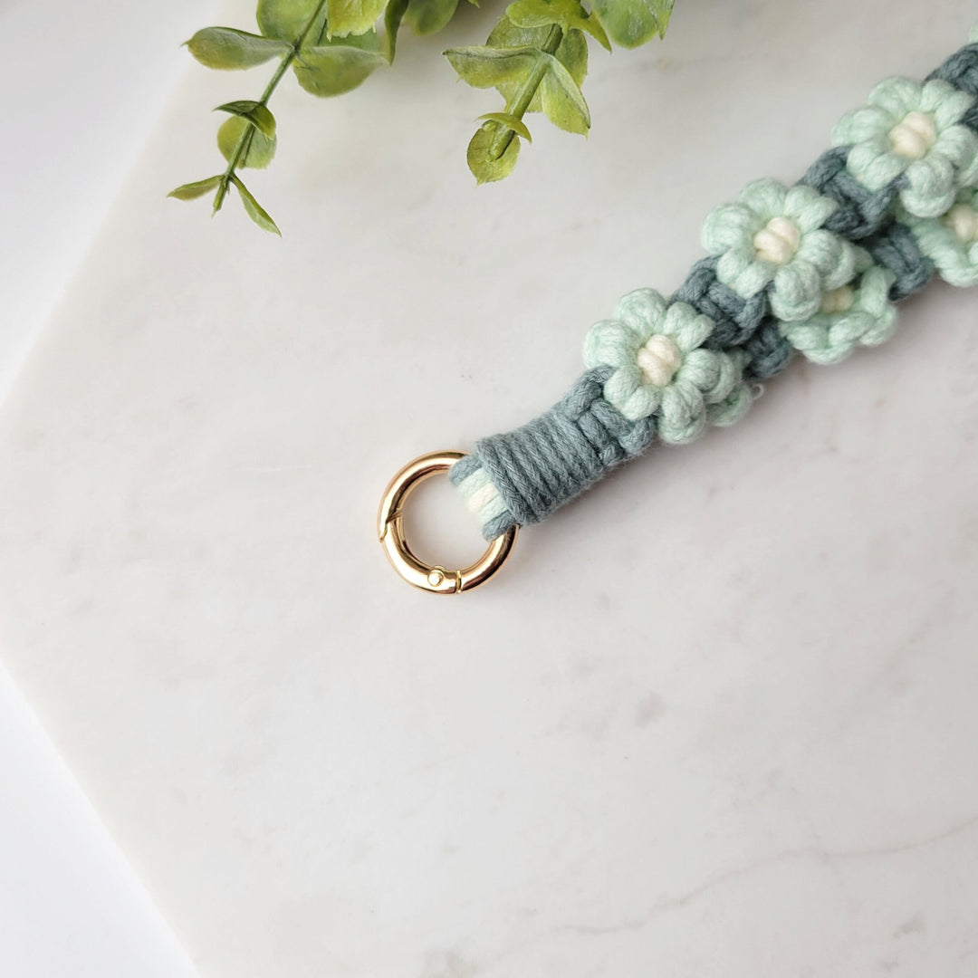 Teal and Blue Flowers Macrame Wristlet Keychain with gold clip, laying on a tile with a close up of the gold clip