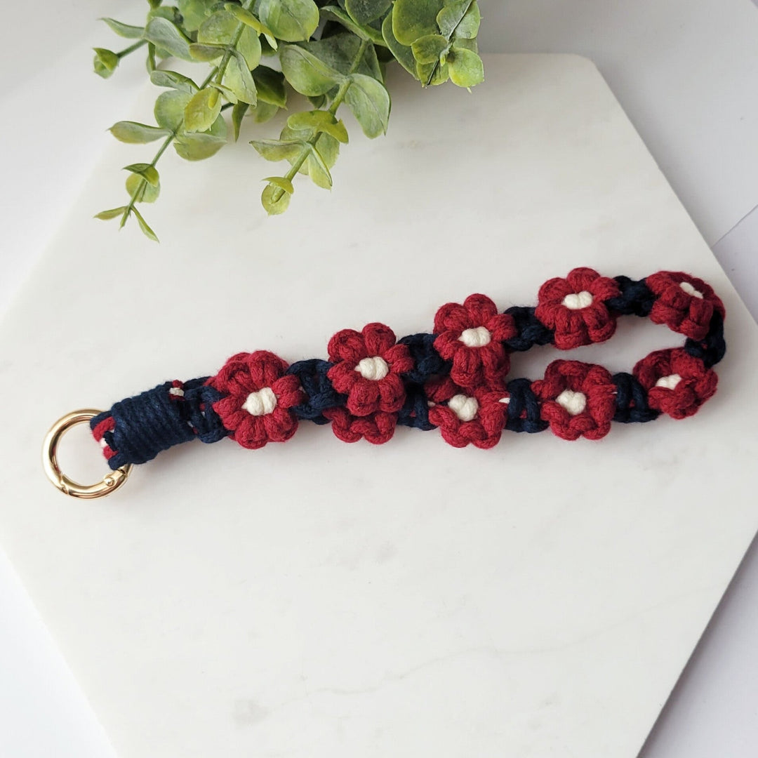 Blue and Maroon Flower Macrame Wristlet Keychain with durable clip for wallets, purses, keys, and bags laying on tile.