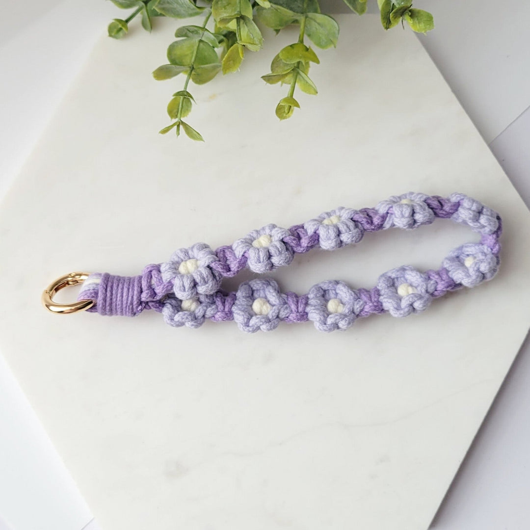 Purple and Lilac Flowers Macrame Wristlet Keychain with gold clip, laying on a tile