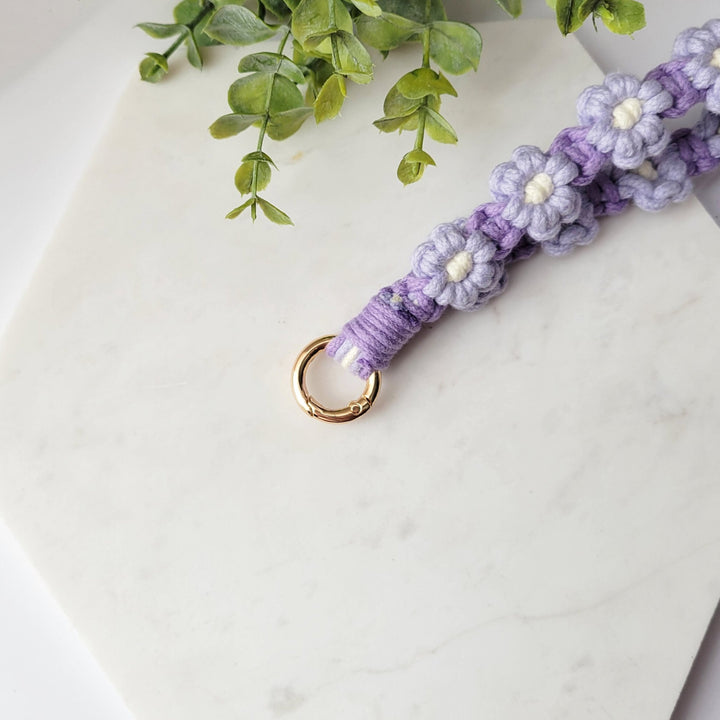 Purple and Lilac Flowers Macrame Wristlet Keychain with gold clip, laying on a tile with a close up of the gold clip