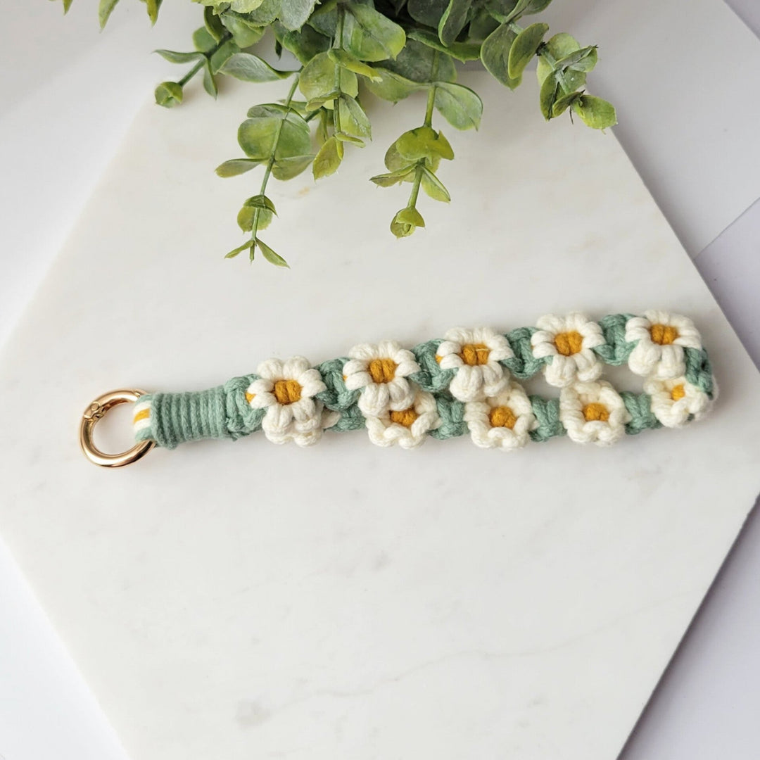 Green and White flowers Macrame Wristlet Keychain with gold clip, laying on a tile