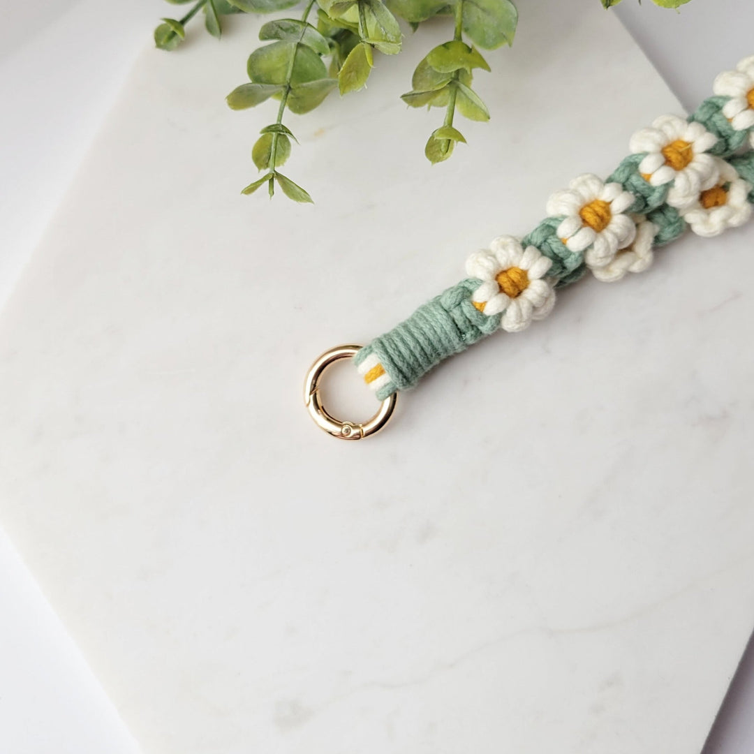 Green and White flowers Macrame Wristlet Keychain with gold clip, laying on a tile with a close up of the gold clip.
