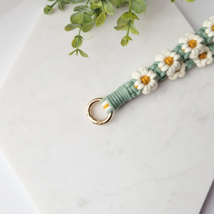 Green and White flowers Macrame Wristlet Keychain with gold clip, laying on a tile with a close up of the gold clip.