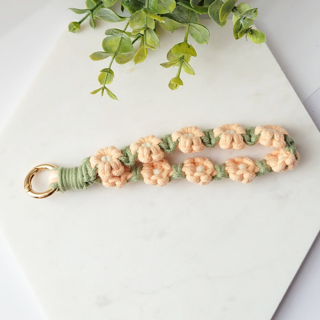 Sage and Pink Flowers Macrame Wristlet Keychain with gold clip, laying on a tile