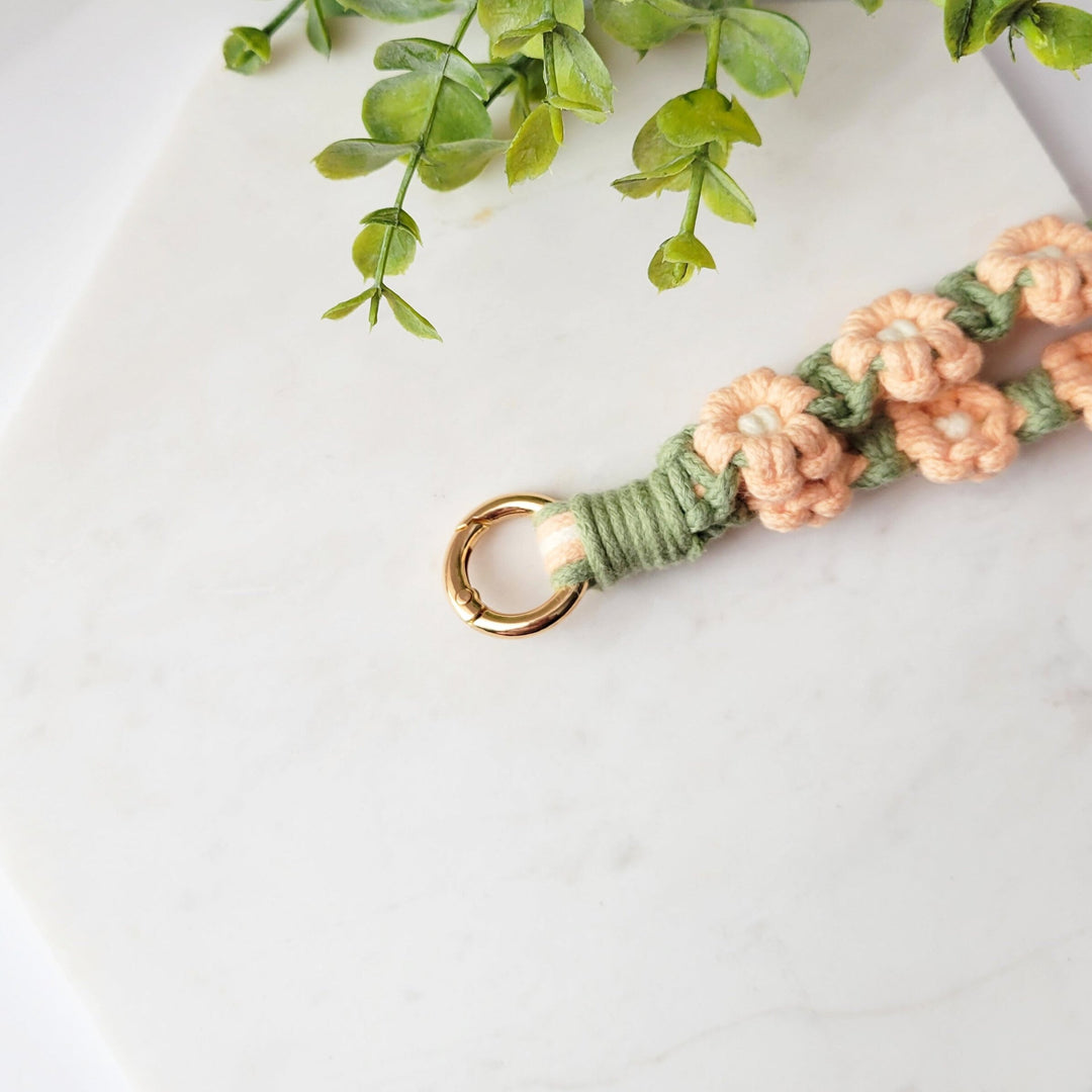 Sage and Pink Flowers Macrame Wristlet Keychain with gold clip, laying on a tile with a close up of the gold clip.