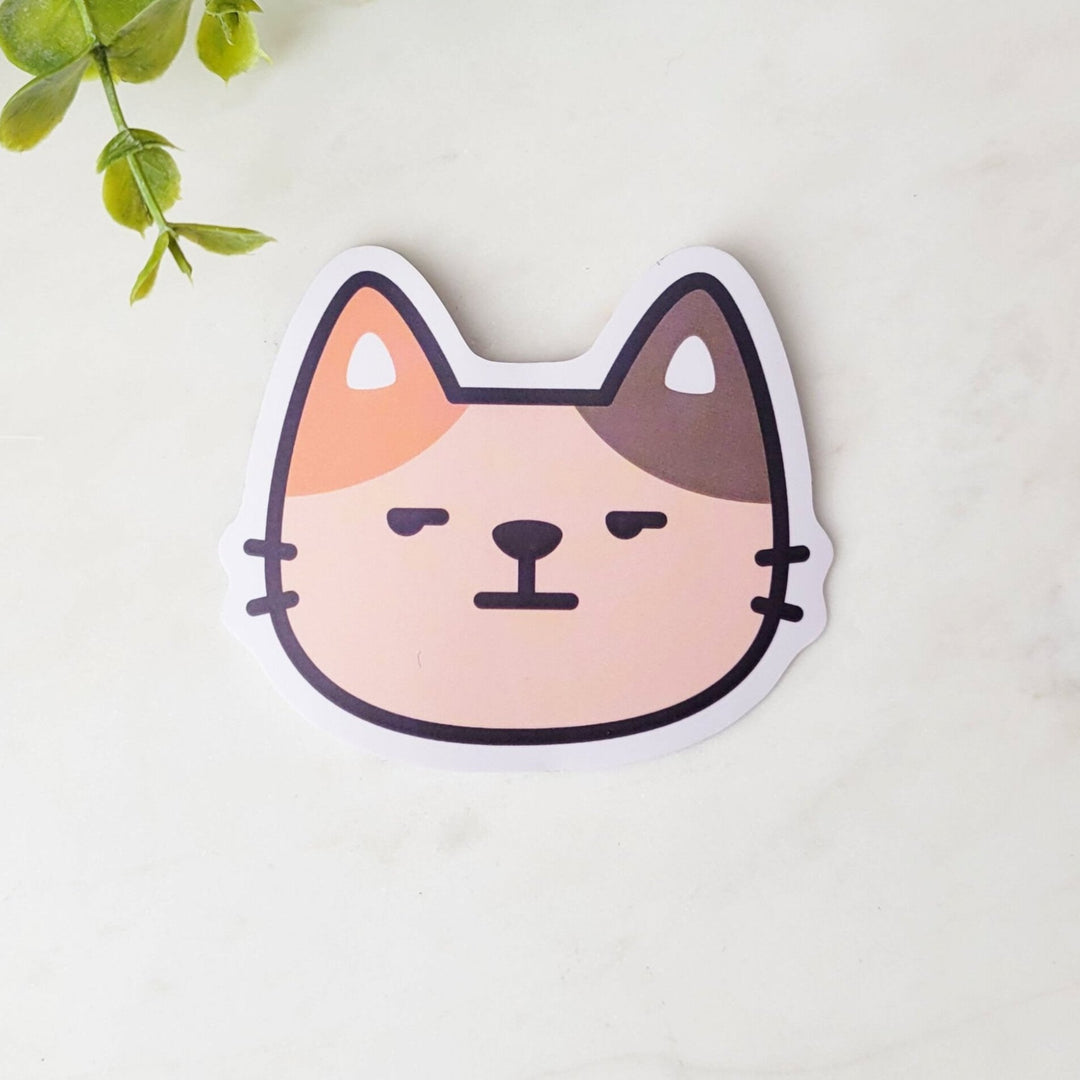 A sticker with a brown and orange cat face, with an annoyed expression.