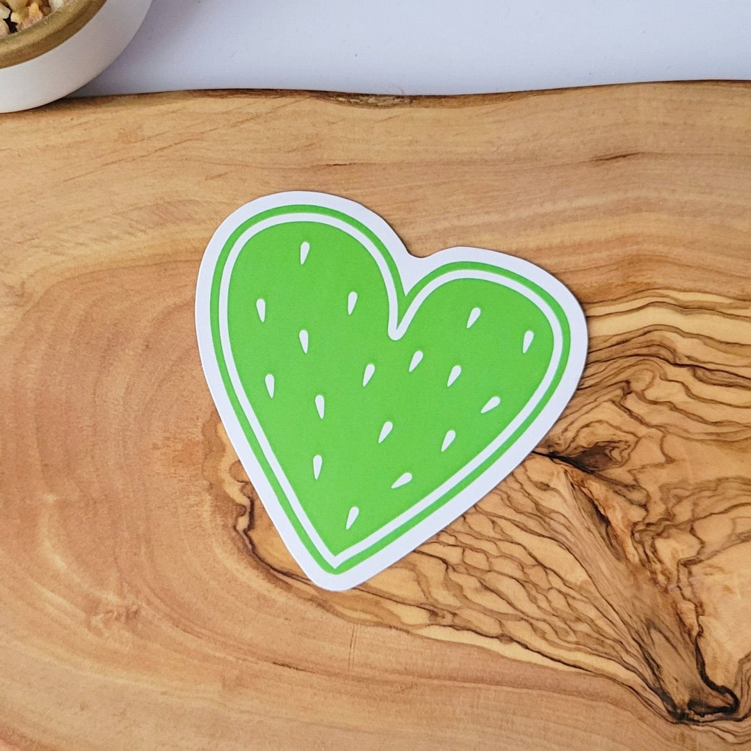a heart shaped sticker, that looks like fruit. it has a green center and white fruit seeds.
