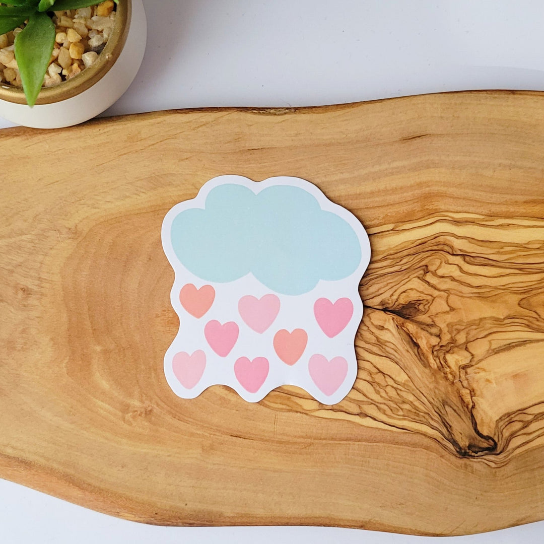 a large sticker of a blue cloud with several pink and salmon colored hearts raining down from the cloud