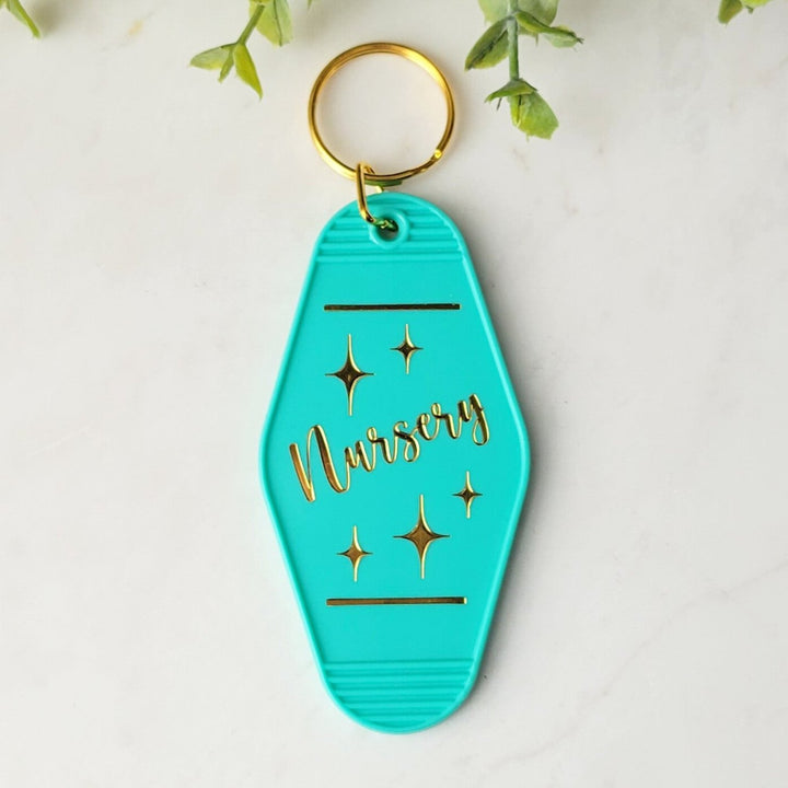 teal colored retro keychain with the words 'Nursery' in gold foil