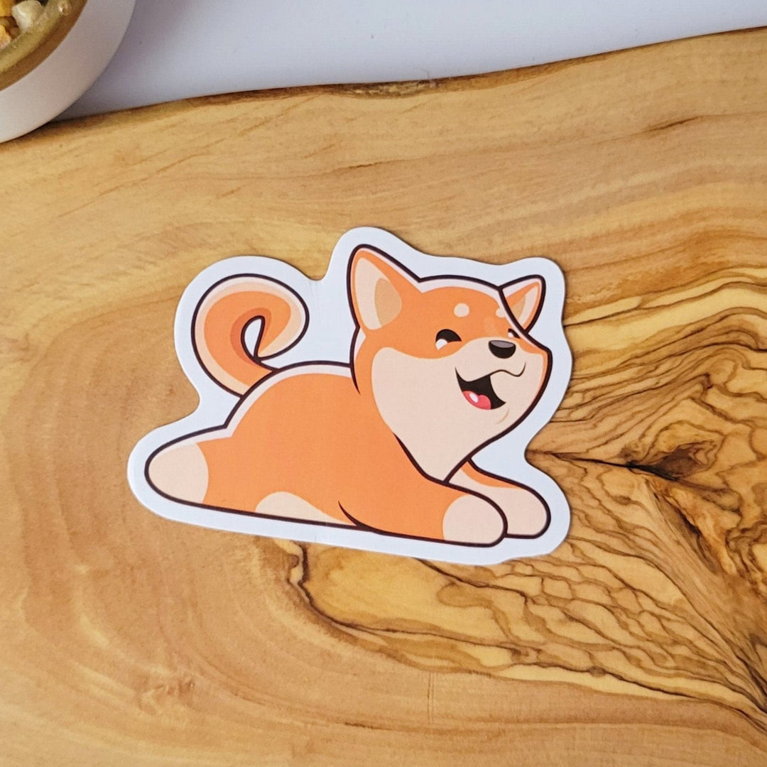 A sticker of a happy orange and tan dog, lying on it's stomach
