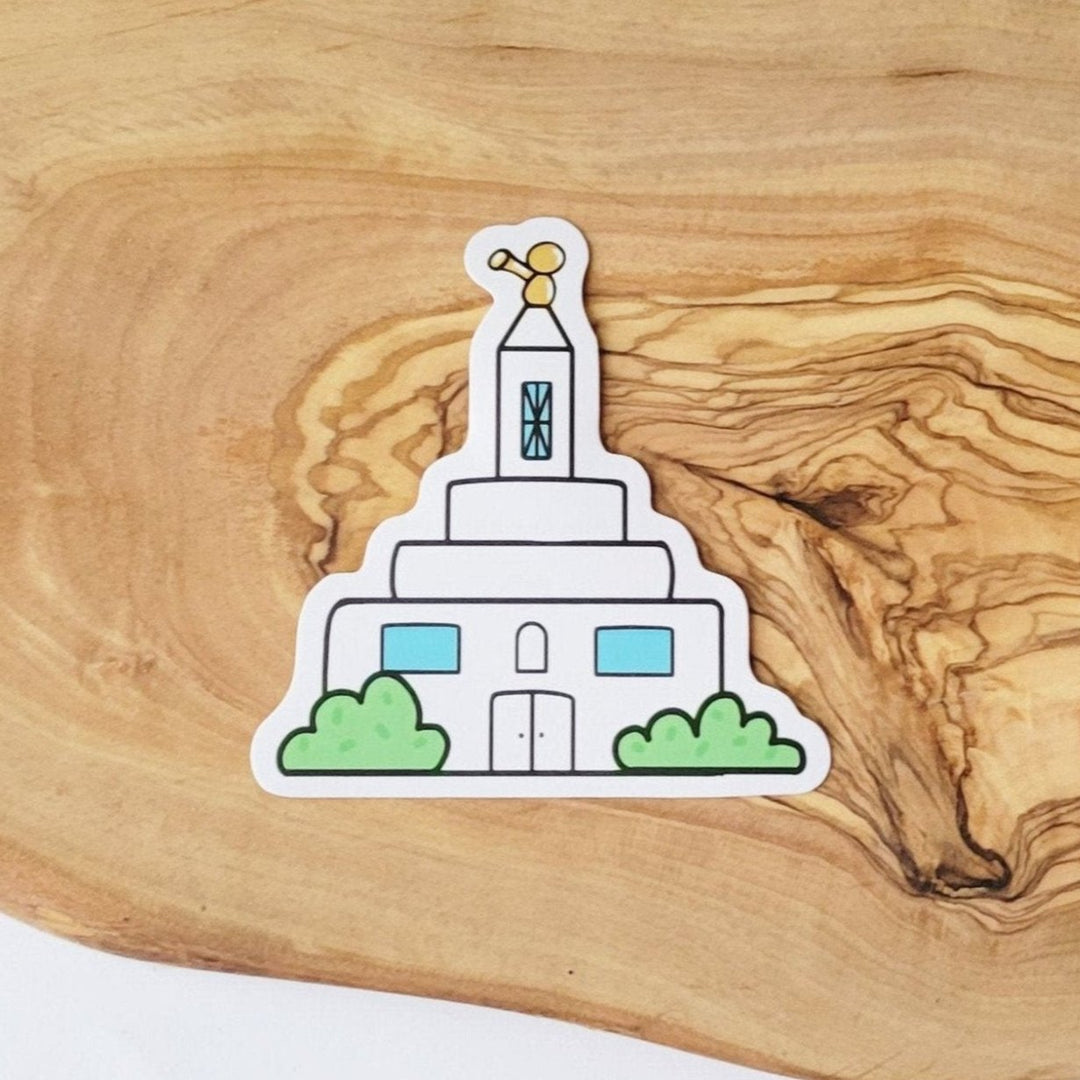 a white LDS temple with green bushes, and small yellow angel Moroni statue on top, in a cartoon style drawing