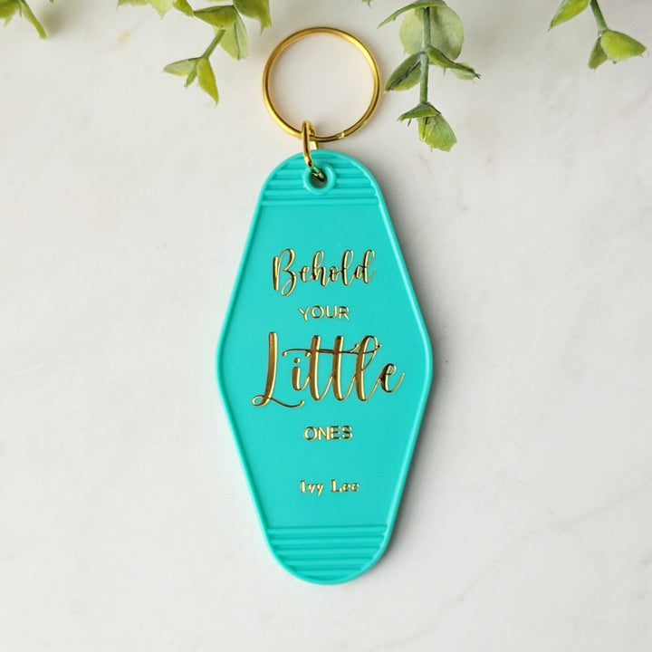 teal colored retro keychain with the words 'Behold your little ones' in gold foil