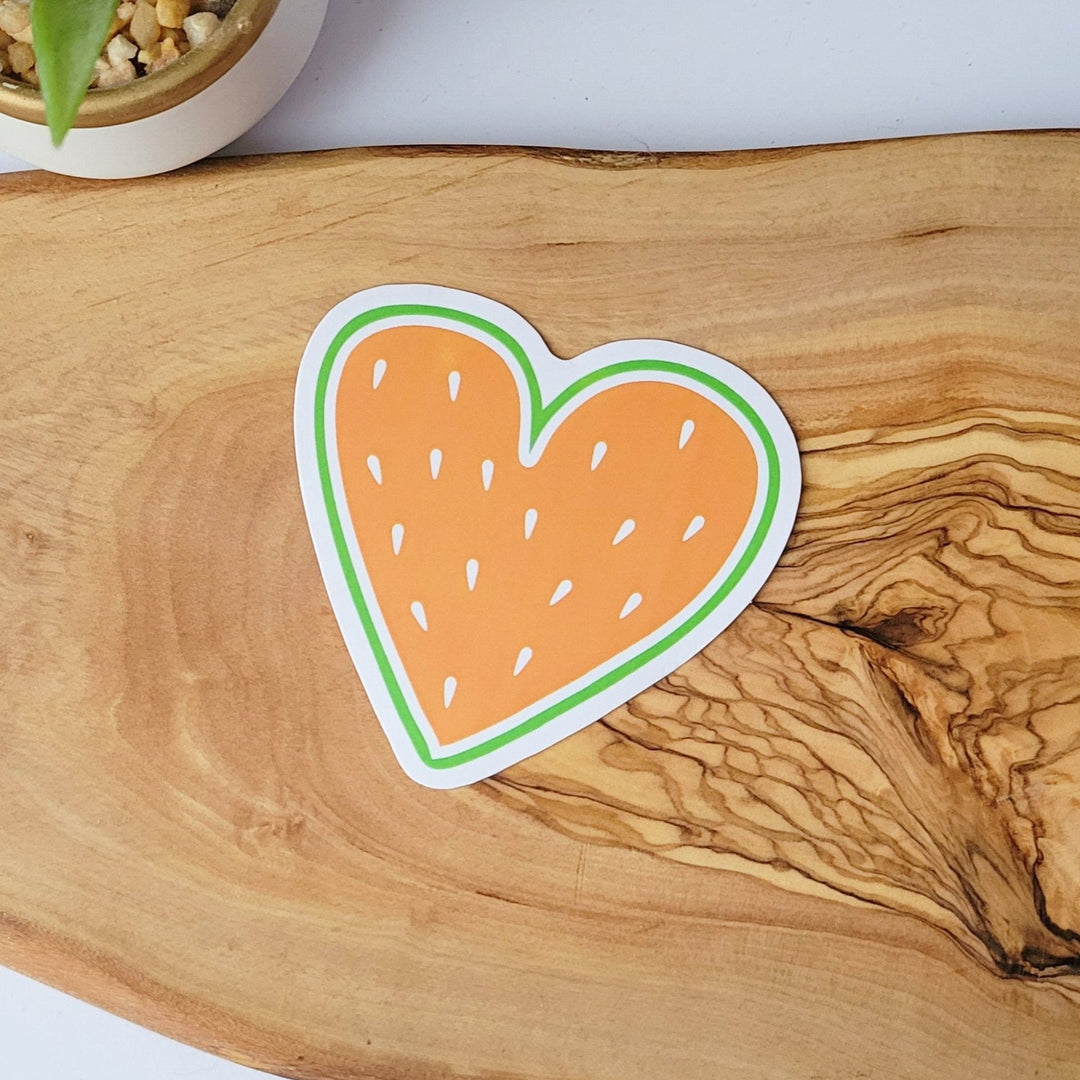 a heart shaped sticker, that looks like fruit. it has an orange center and white fruit seeds.