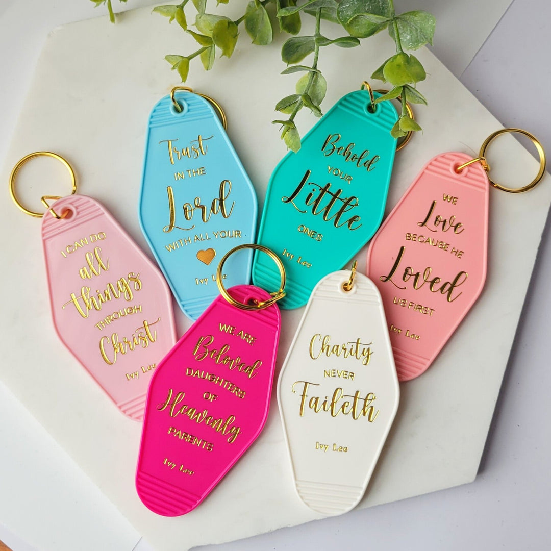 a group of retro style motel keychains, with gold rings, with several says on the backs. 'I can do all things through Christ', 'Trust in the Lord with all your Heart', 'Behold your little ones', 'We love because He loved us first', 'We are beloved daughters of Heavenly Parents', and 'Charity never Faileth'.