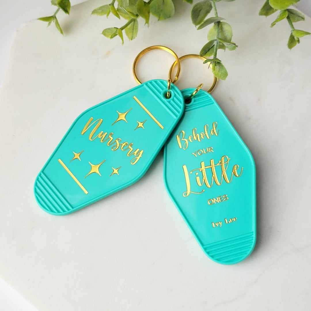 teal colored retro keychain with the words 'Nursery' in gold foil, and a second one with 'Behold Your little ones Ivy lee'