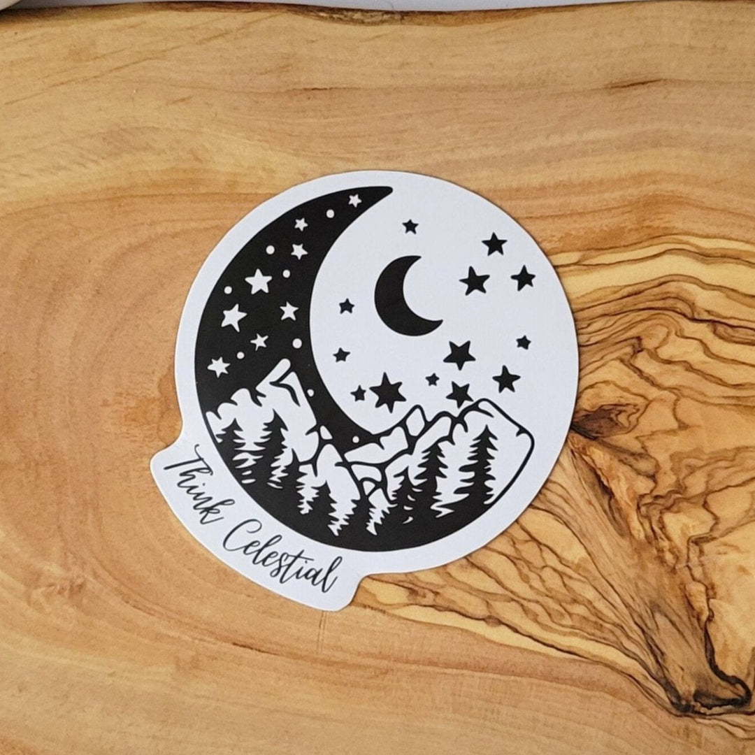 A black and white sticker, with a crescent shaped moon depicting mountains and trees, with a moon and stars, and Think Celestial