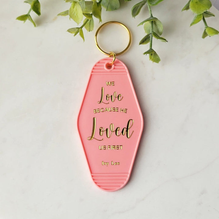 salmon pink keychain with 'We love Because He loved us first" in gold foil