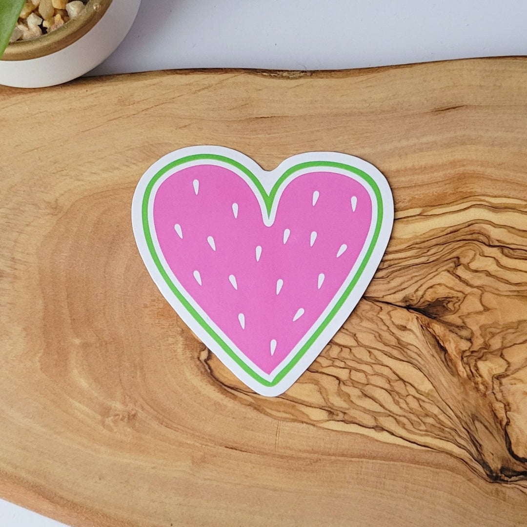 a heart shaped sticker, that looks like fruit. it has a pink center and white fruit seeds.