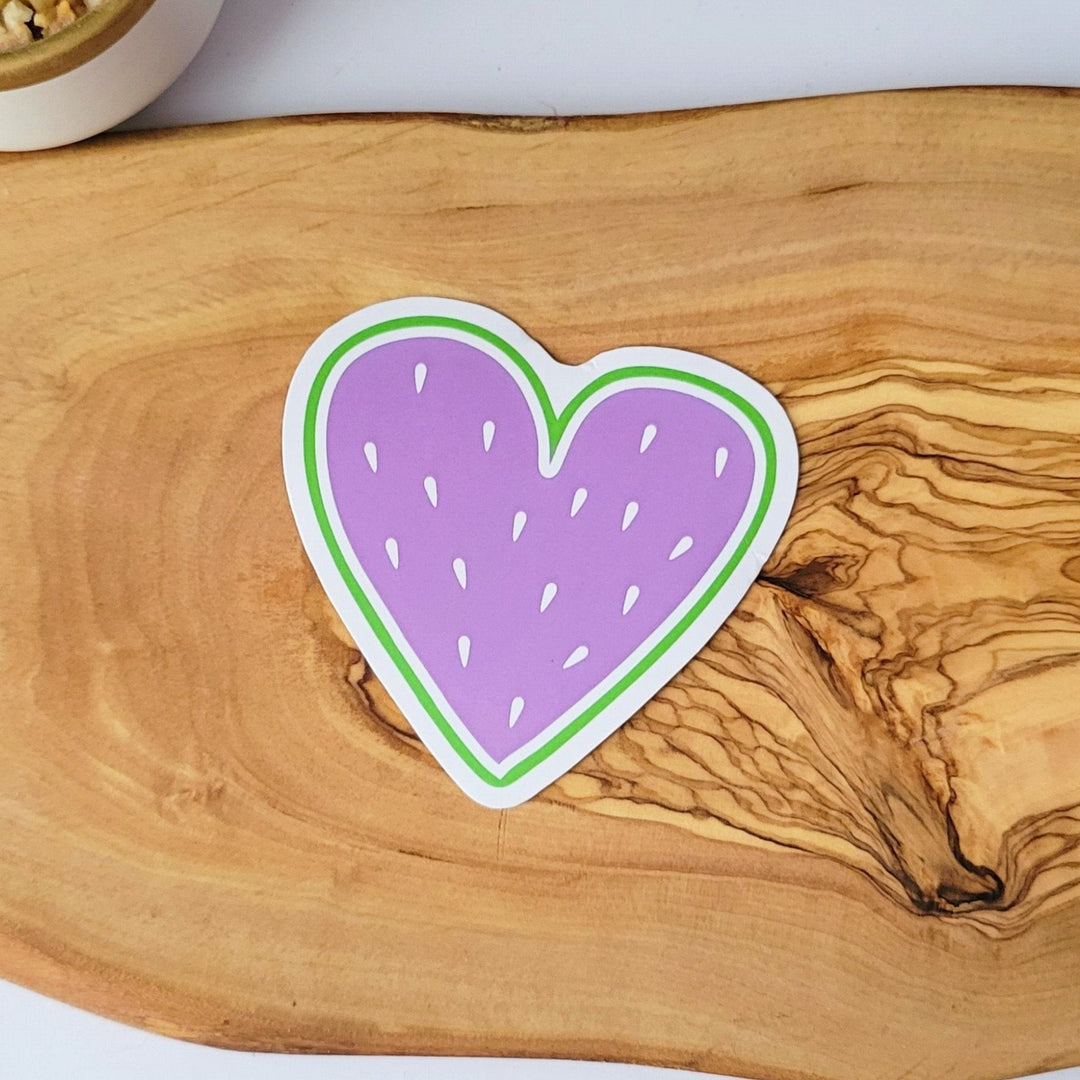 a heart shaped sticker, that looks like fruit. it has a purple center and white fruit seeds.