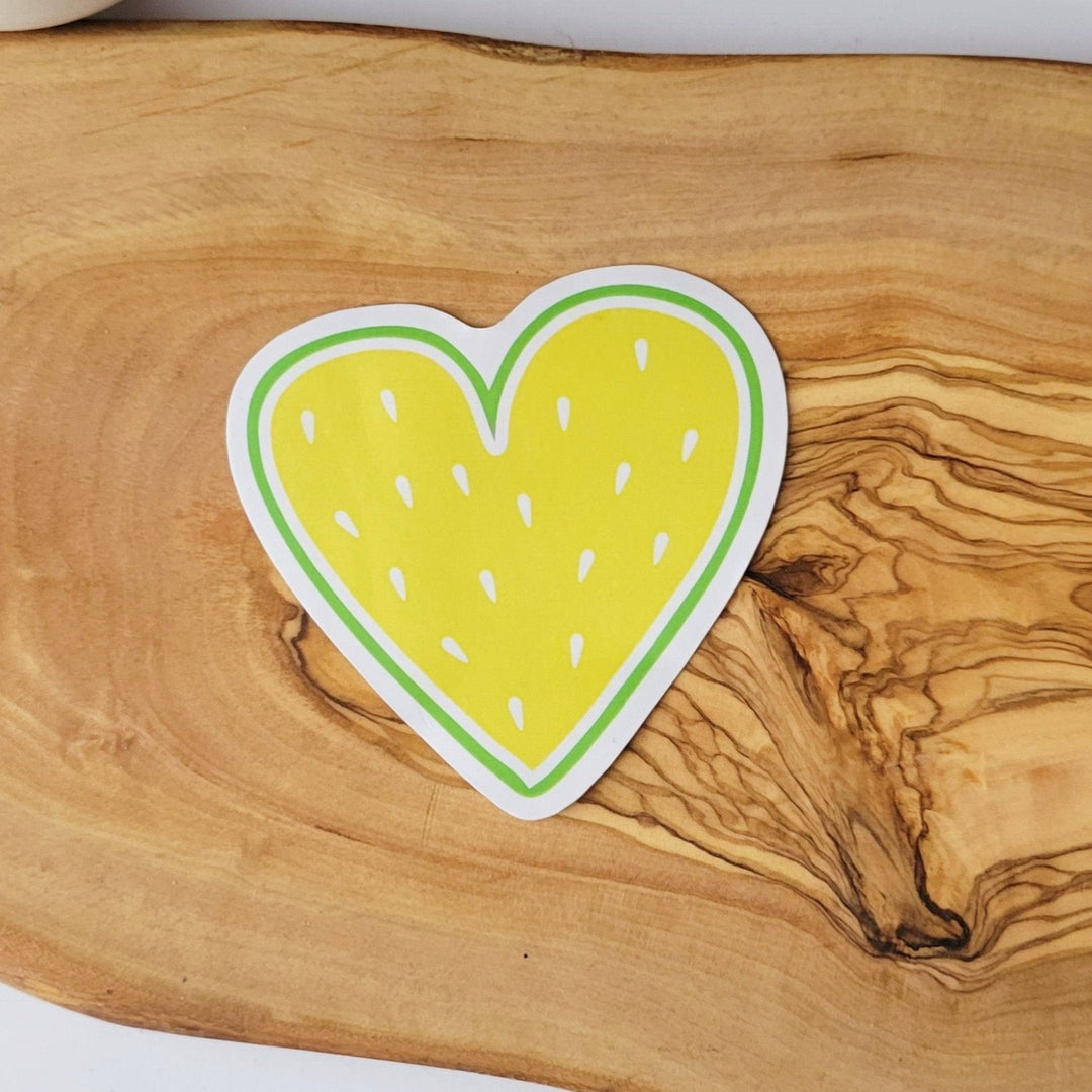 A heart shaped sticker that looks like fruit. It has a yellow center, with white seeds.