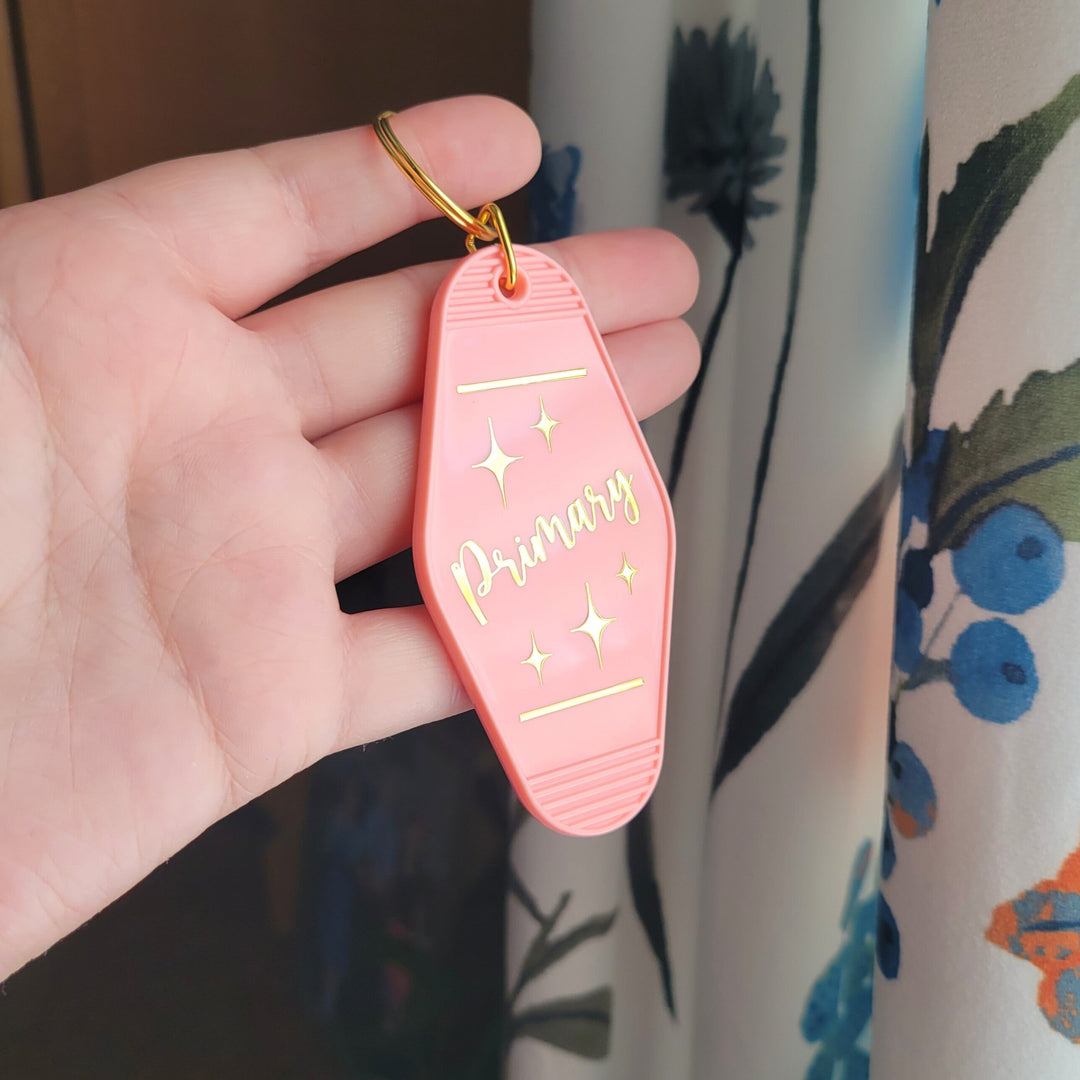 retro shape salmon pink keychain, with 'Primary' in gold foil being held up