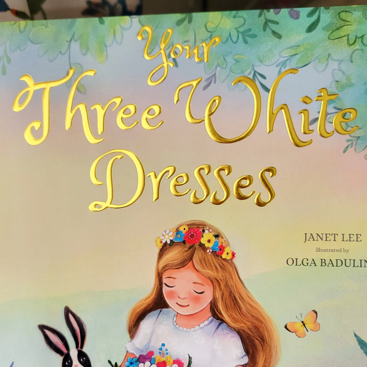 Book cover of 'Your Three White Dresses' with a girl in a white dress holding flowers, surrounded by butterflies and flowers.