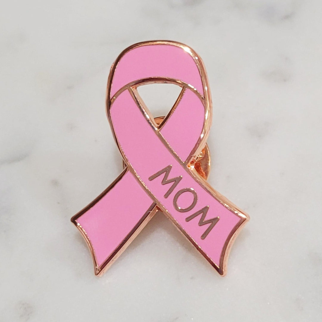 close up of the words mom on a breast cancer enamel pin